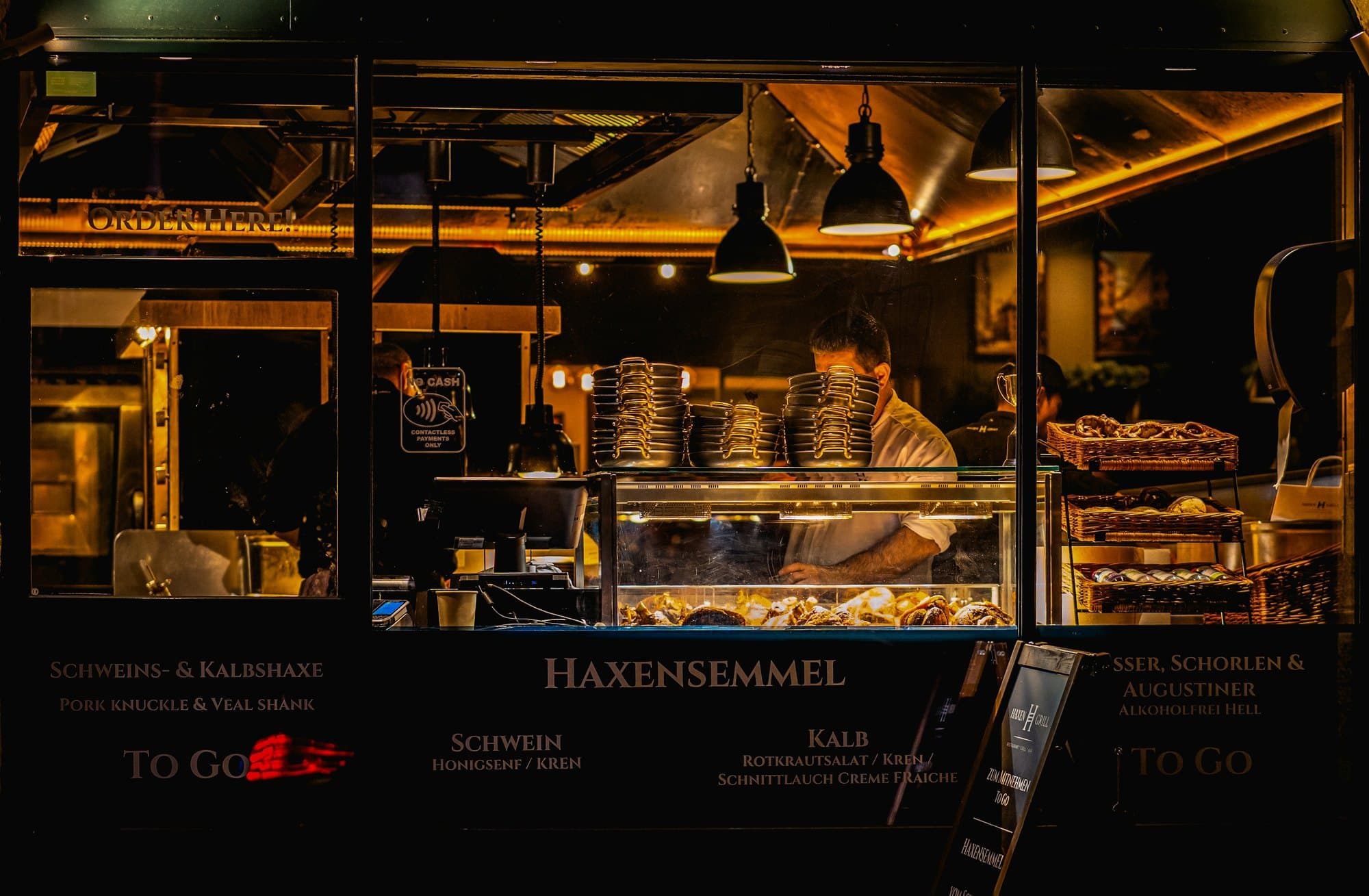 A baker working behind a lit counter at night, trays of pastries stacked in the case in front of him