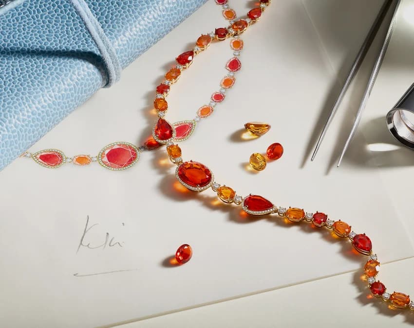 A Kiki McDonough fire opal and diamond necklace beside loose gemstones and a design sketch