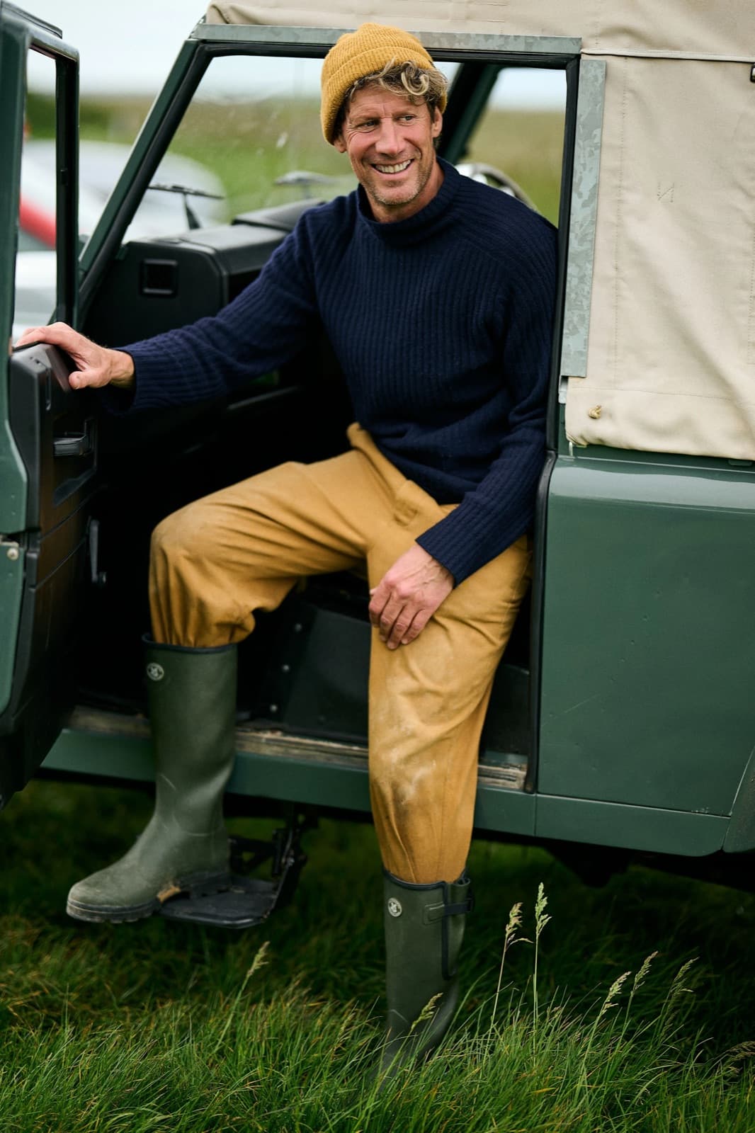 A man in Le Chameau wellington boots sitting in the doorway of a Land Rover on the marsh