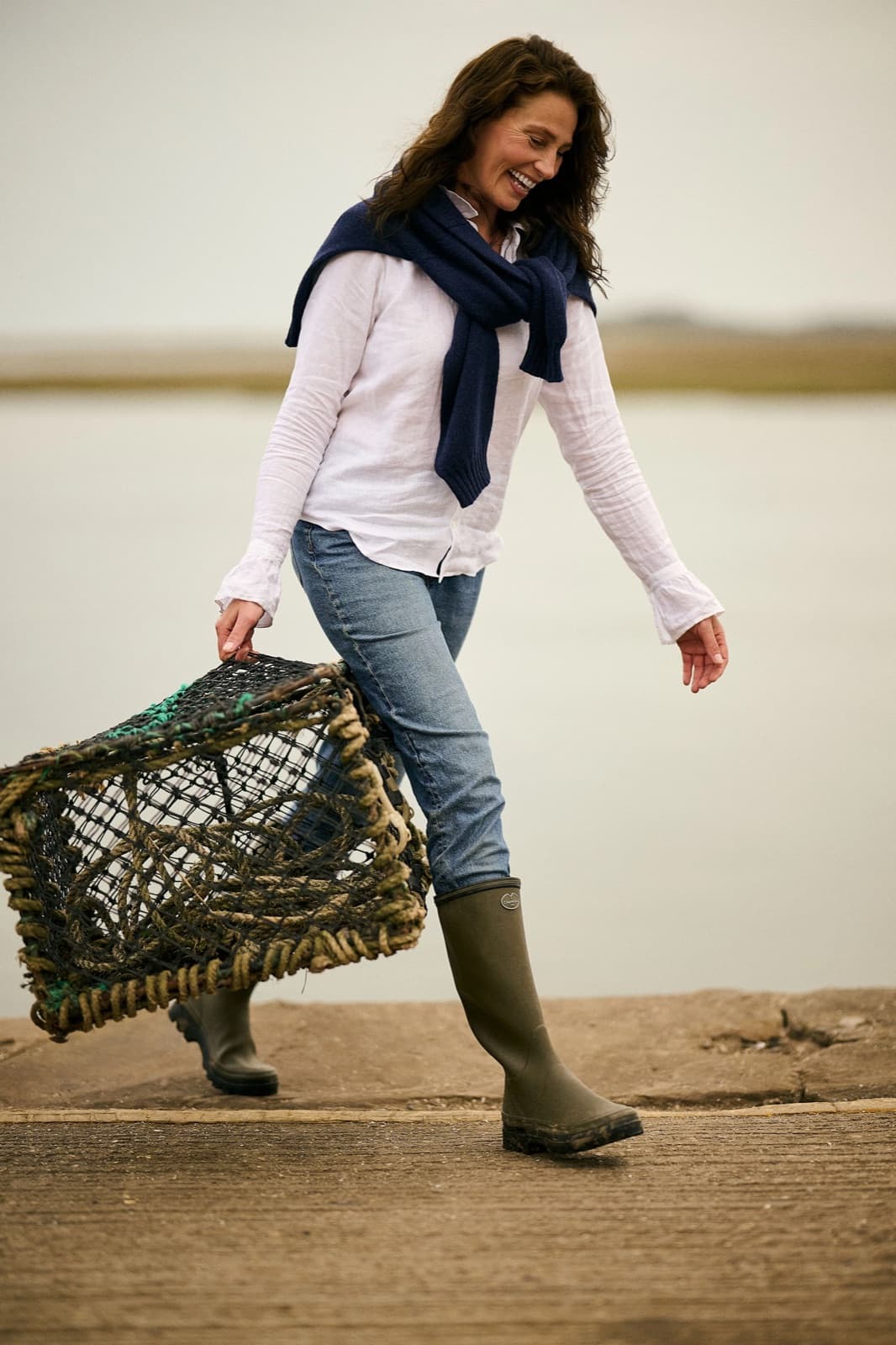 A woman carrying a lobster pot along a harbour quay in Le Chameau wellington boots