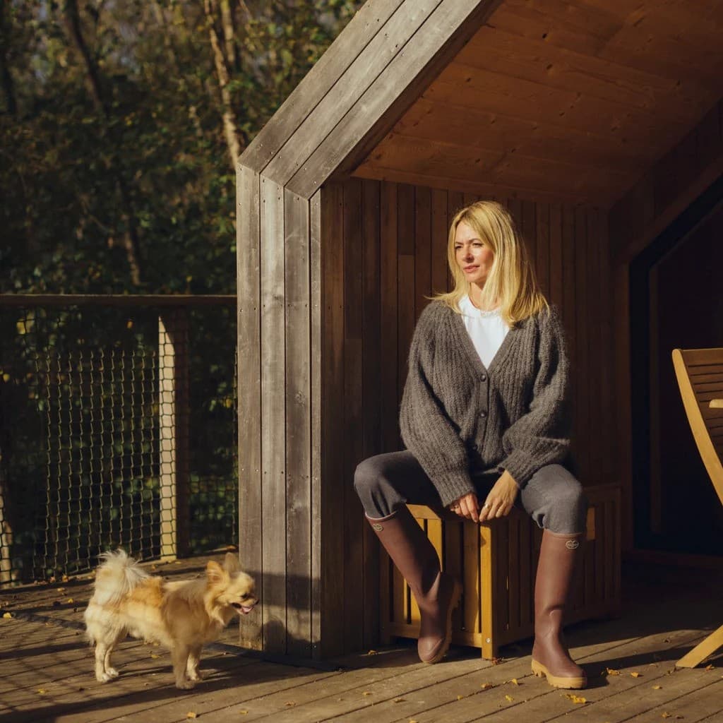 A woman in Le Chameau boots on a cabin porch, a dog beside her