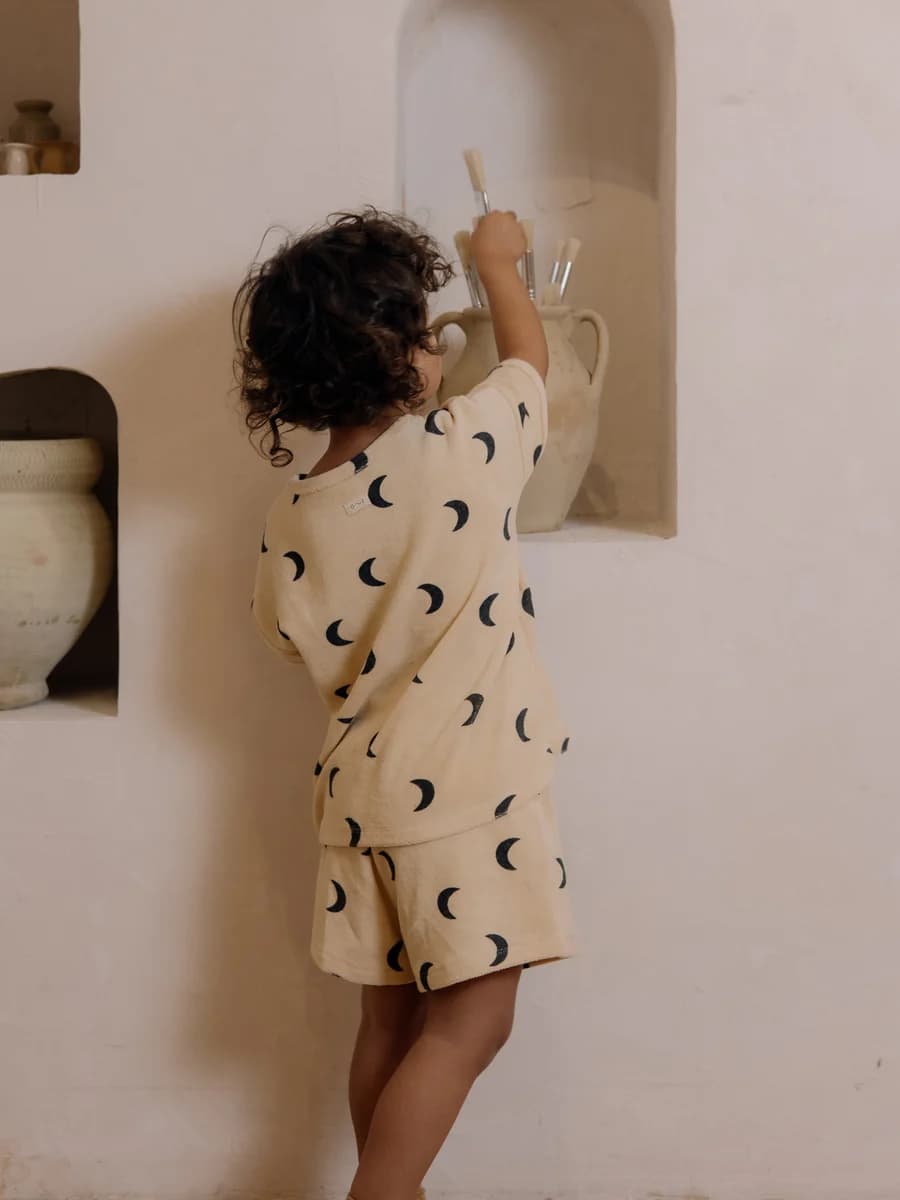 A child in an Organic Zoo moon-print pyjama set, reaching for paintbrushes