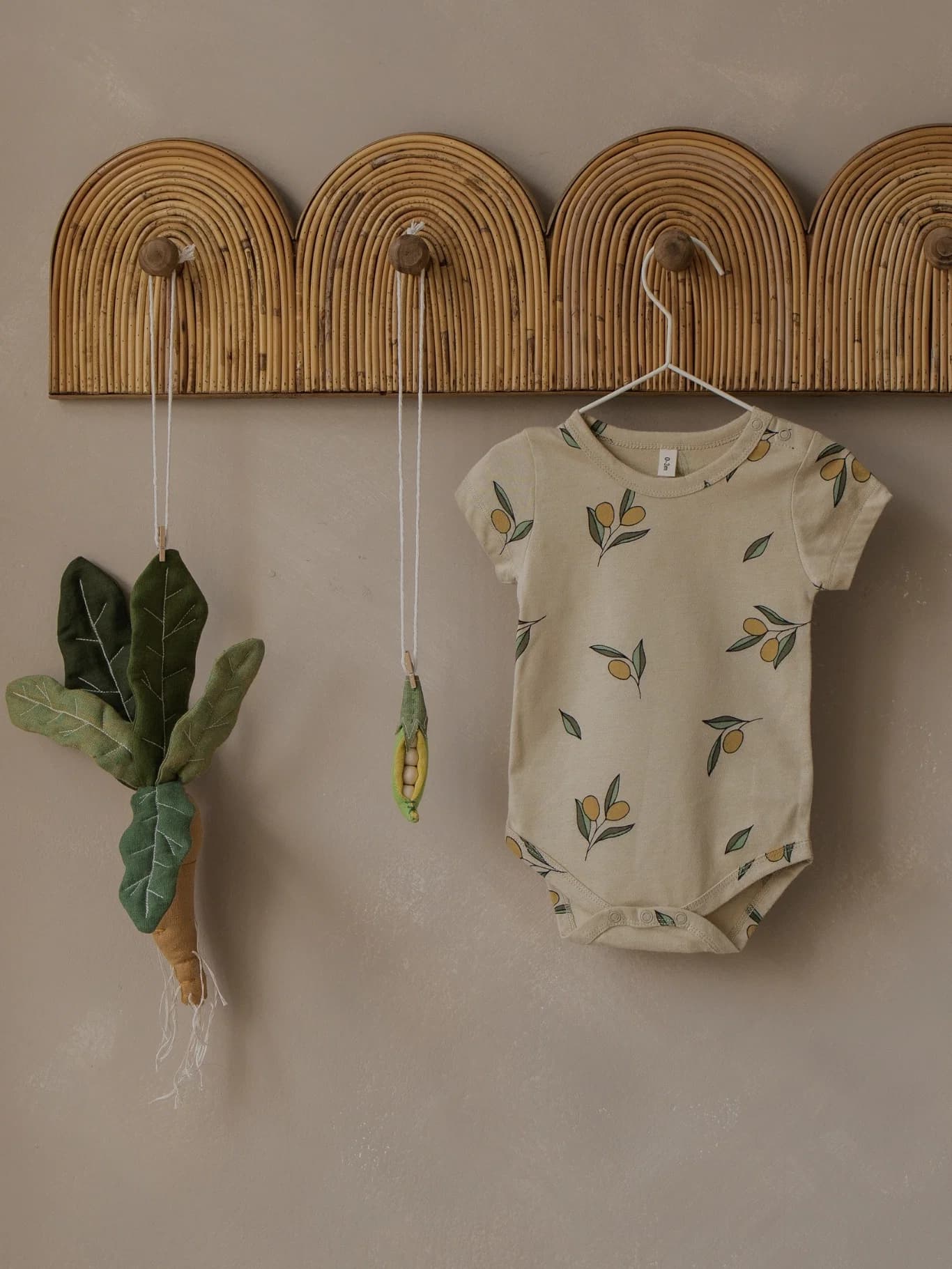 An Organic Zoo olive garden print bodysuit hanging beside knitted toys