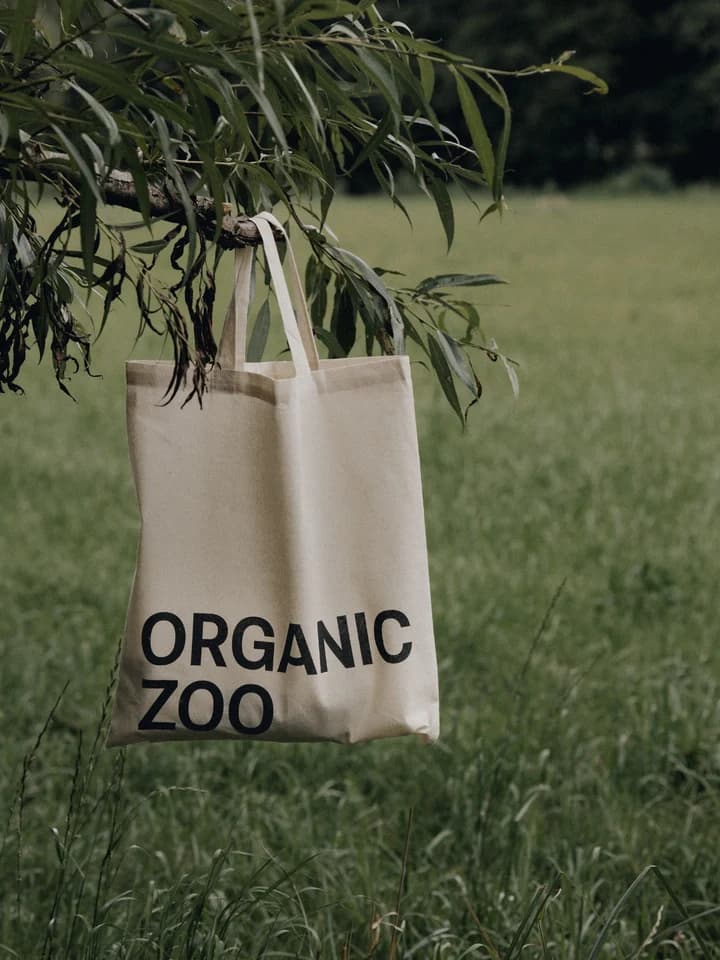 An Organic Zoo tote bag hanging from a tree branch