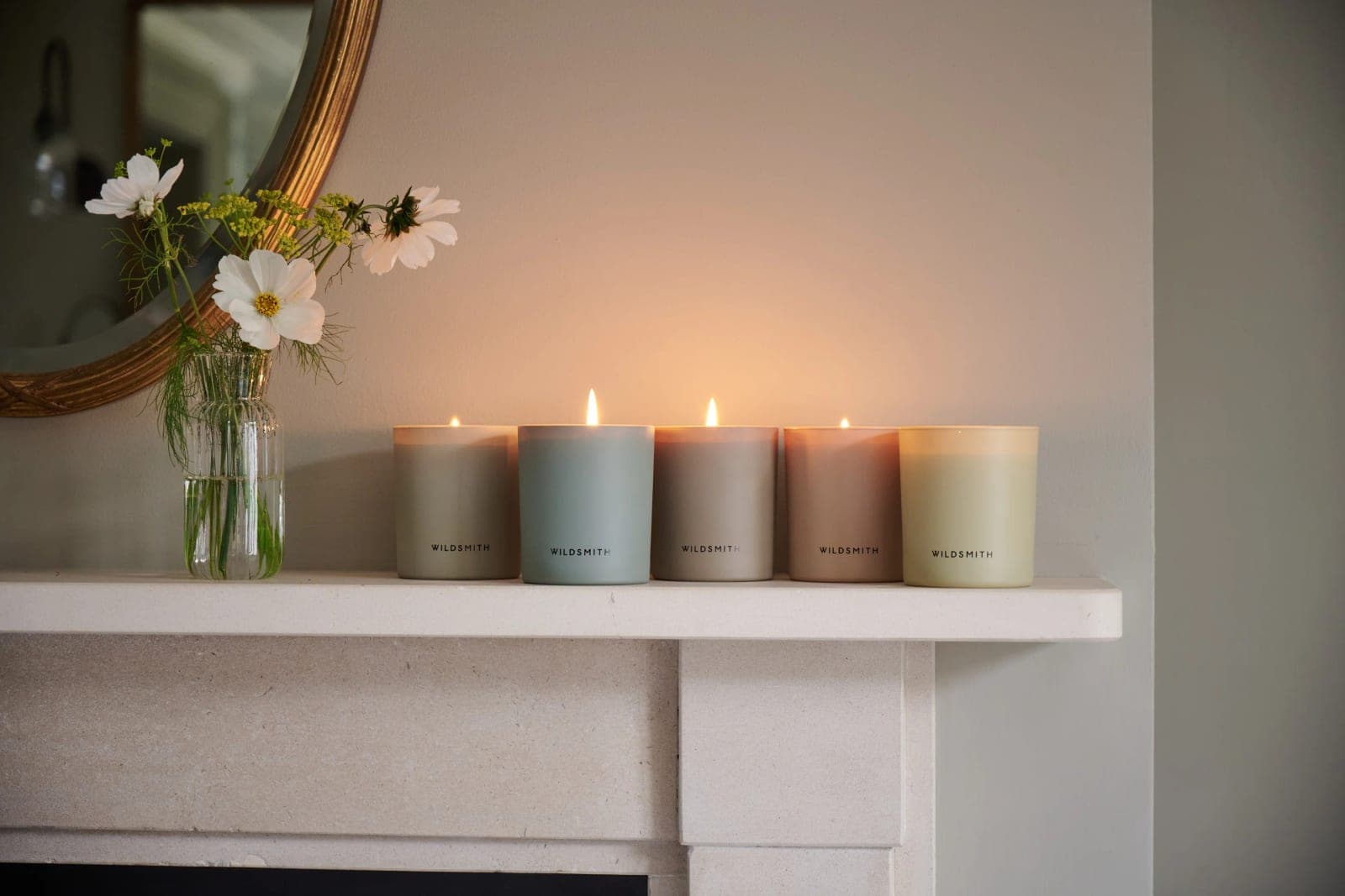 Five Wildsmith candles lit along a stone mantelpiece