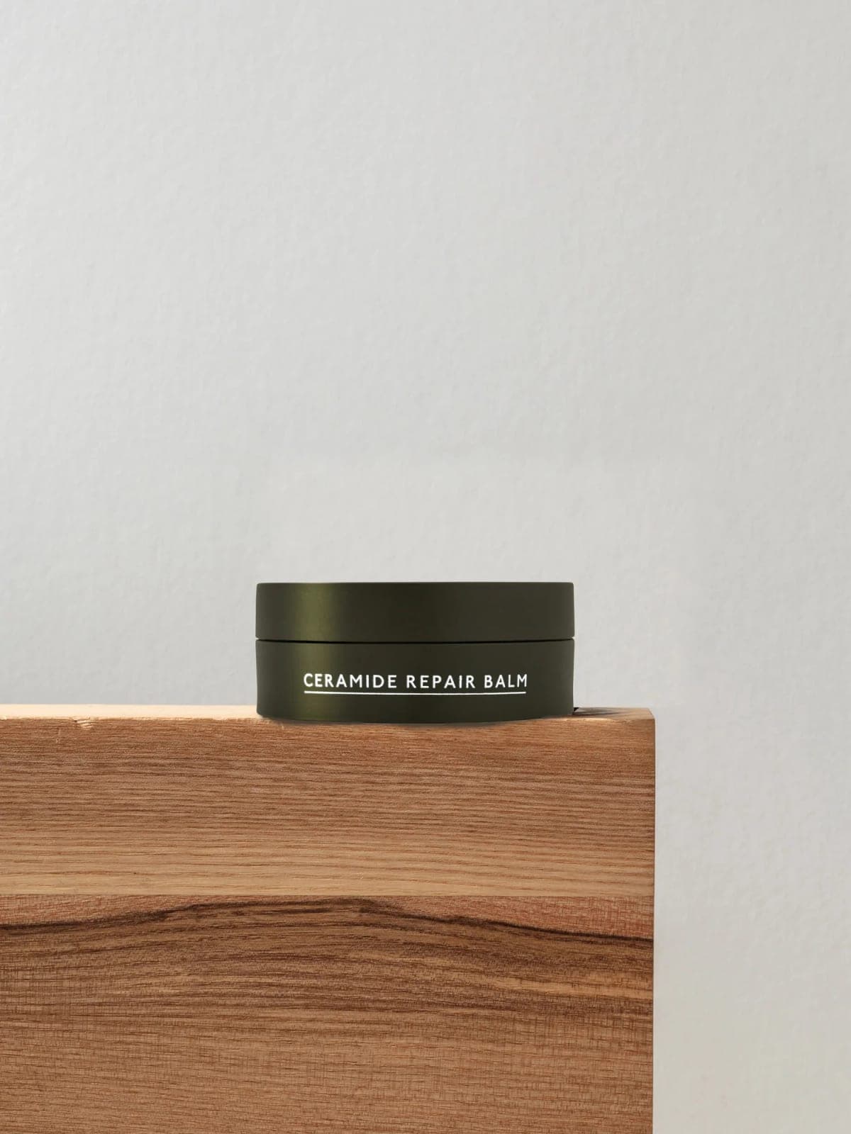 Wildsmith Skin Ceramide Repair Balm in its compostable Vivomer jar, on a block of oak