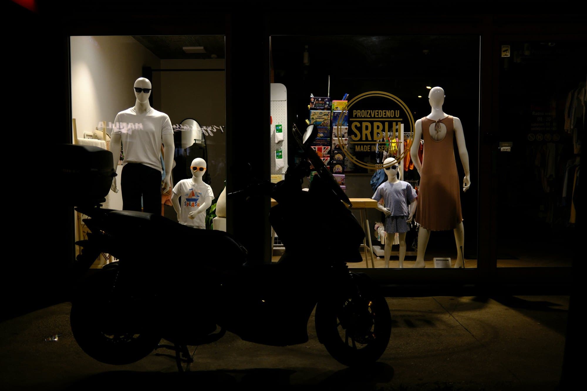 A lit shop window seen from the dark street, a parked scooter cutting across the display