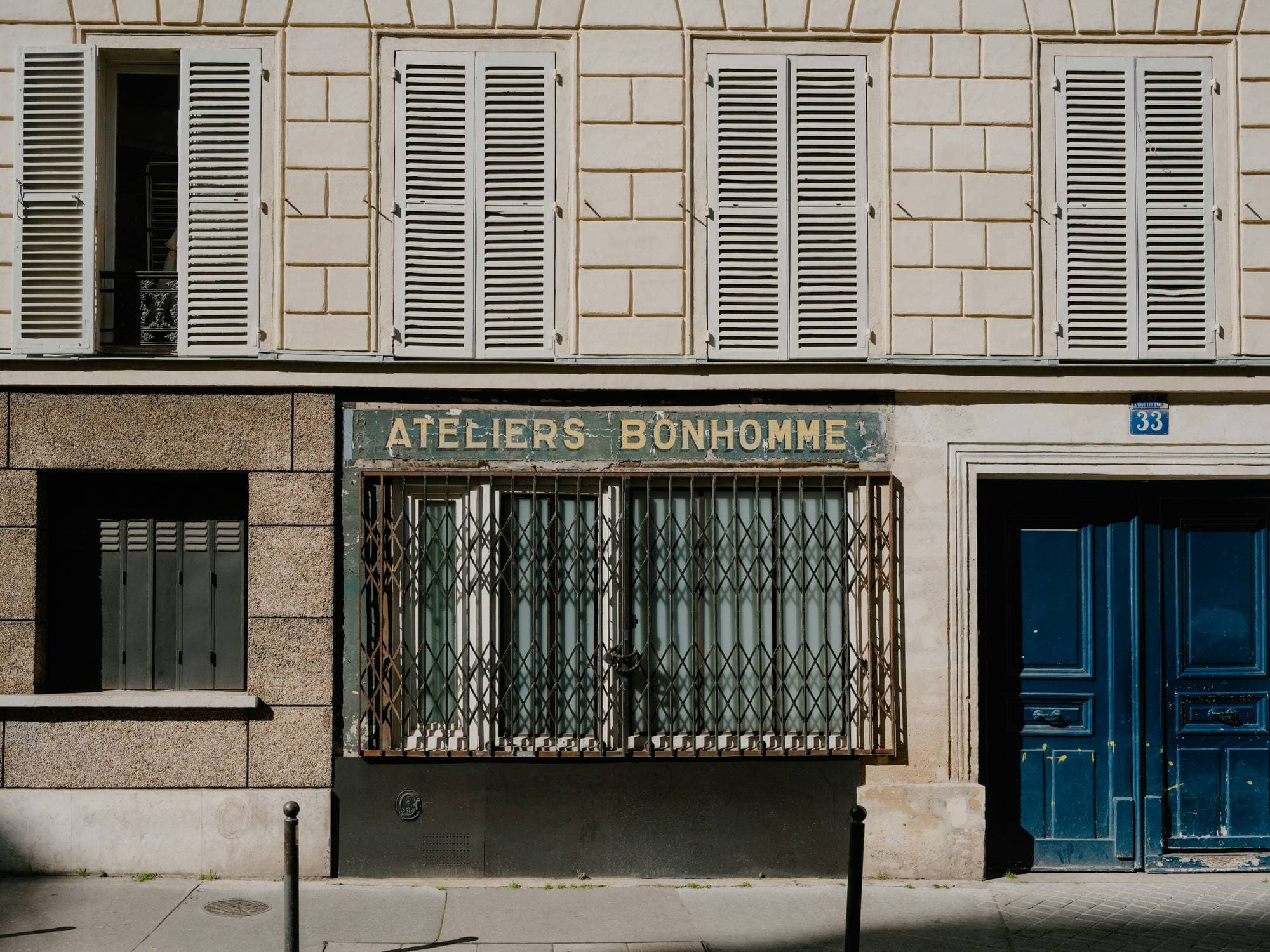 A small workshop front on a quiet Paris street, its name painted above a folding metal grille