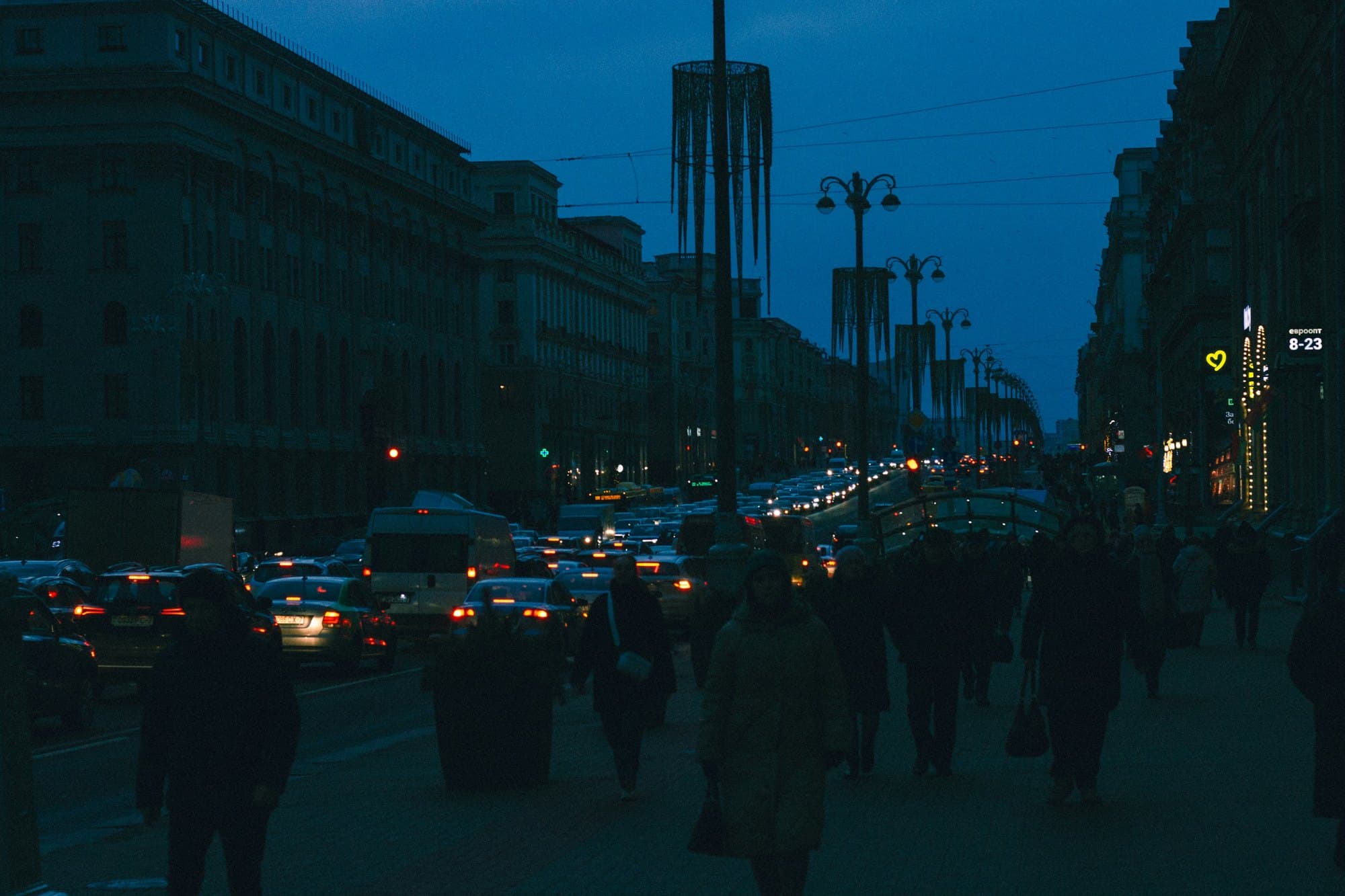 Pedestrians and traffic filling a city boulevard at dusk, the crowd silhouetted against the lights