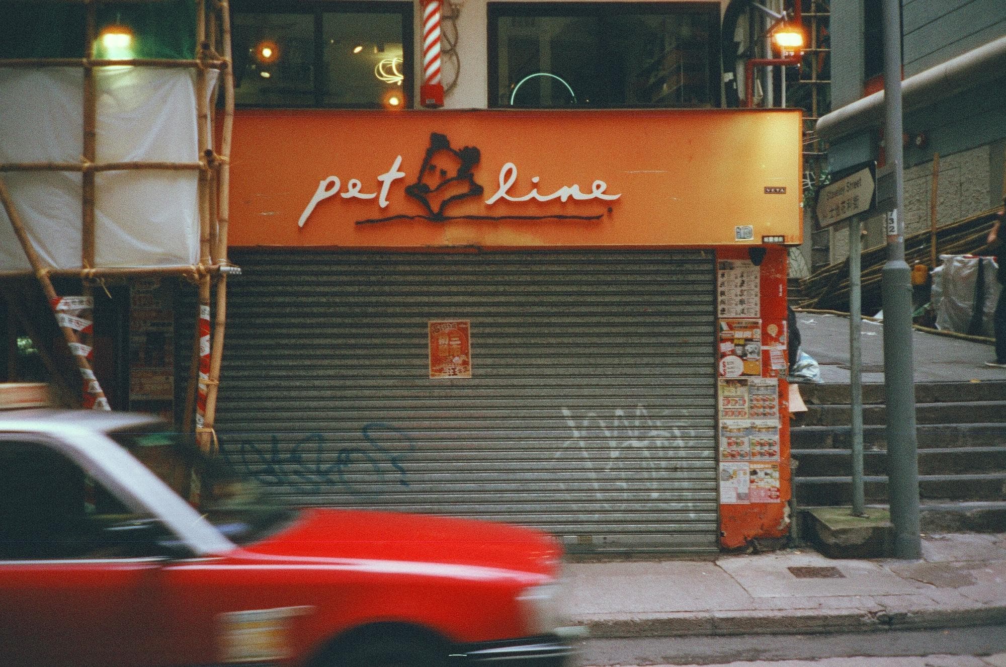 A red Hong Kong taxi blurring past a shop with its shutter pulled down