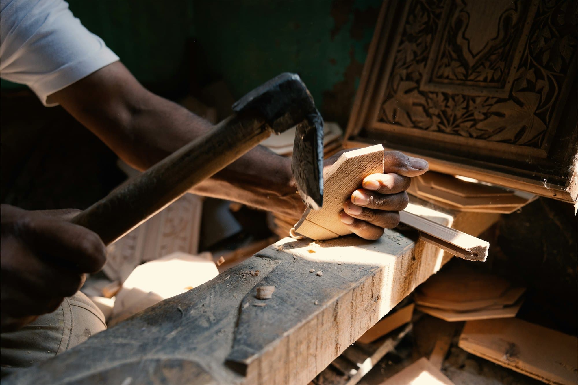 A craftsman's hands guiding a chisel and mallet through a block of wood on a workbench
