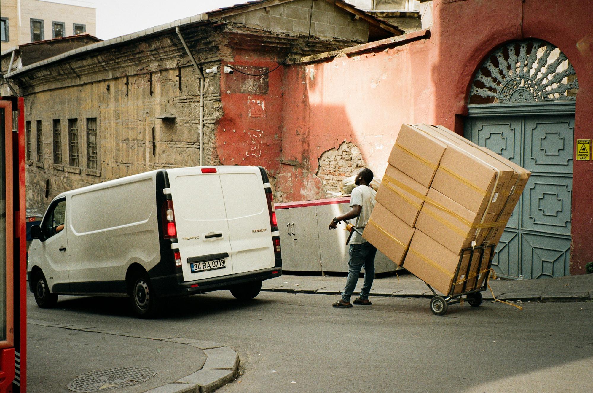 A man steadying a tall stack of taped boxes on a sack truck as he wheels them away from a van