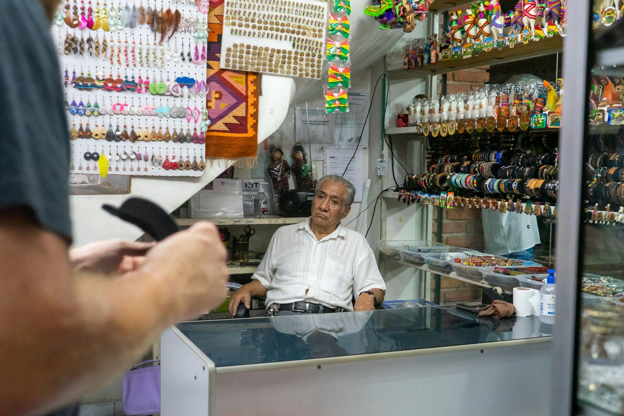 A customer at a market stall counter, asking the trader for something across a glass display case