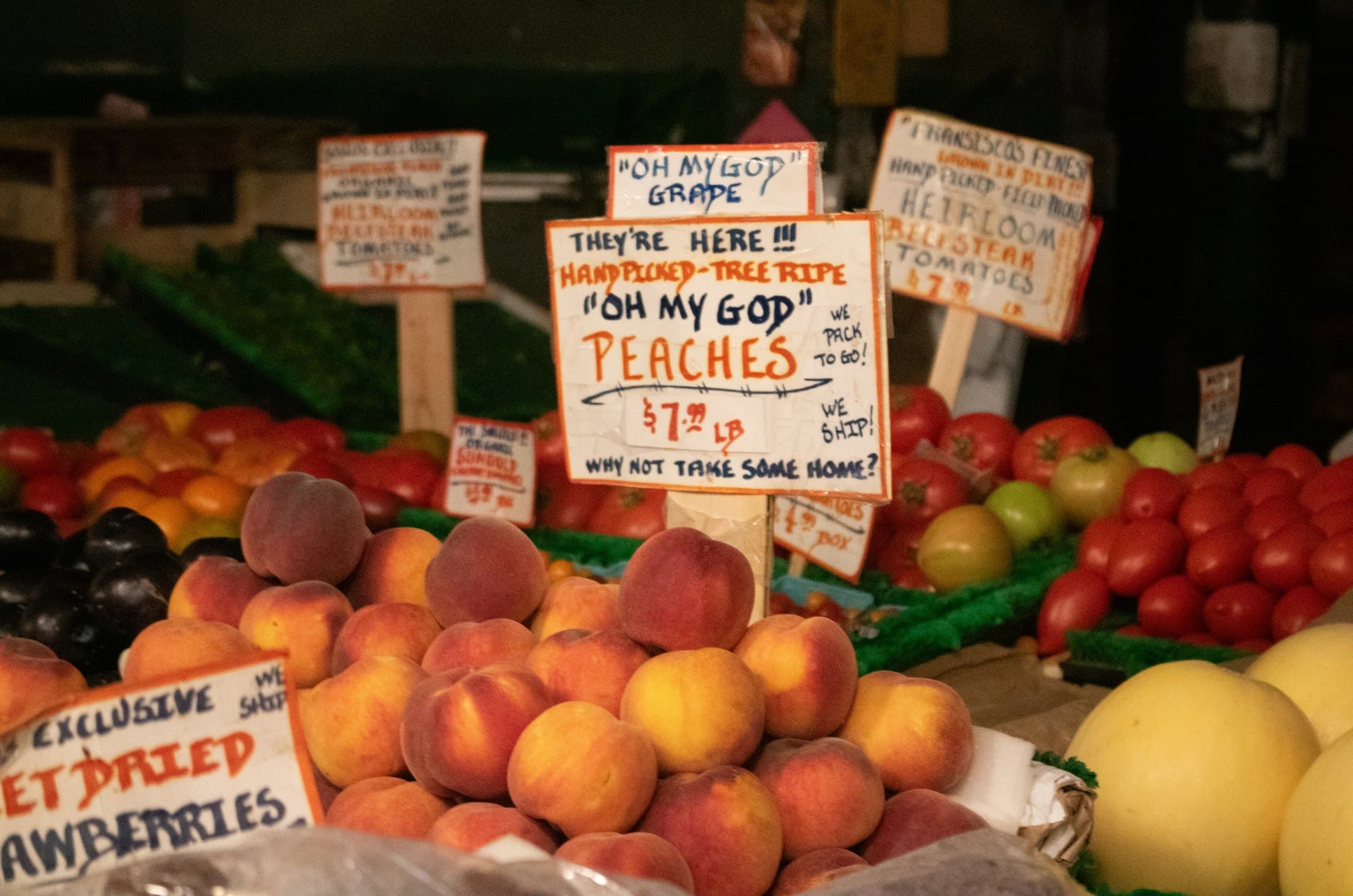 Peaches and tomatoes on a market stall, each variety named and priced on its own handwritten card